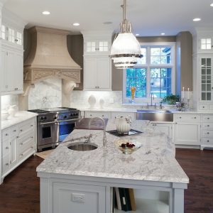 Luxurious white marble residential kitchen with hardwood floors, stainless steel appliances, and white enamel custom cabinets.